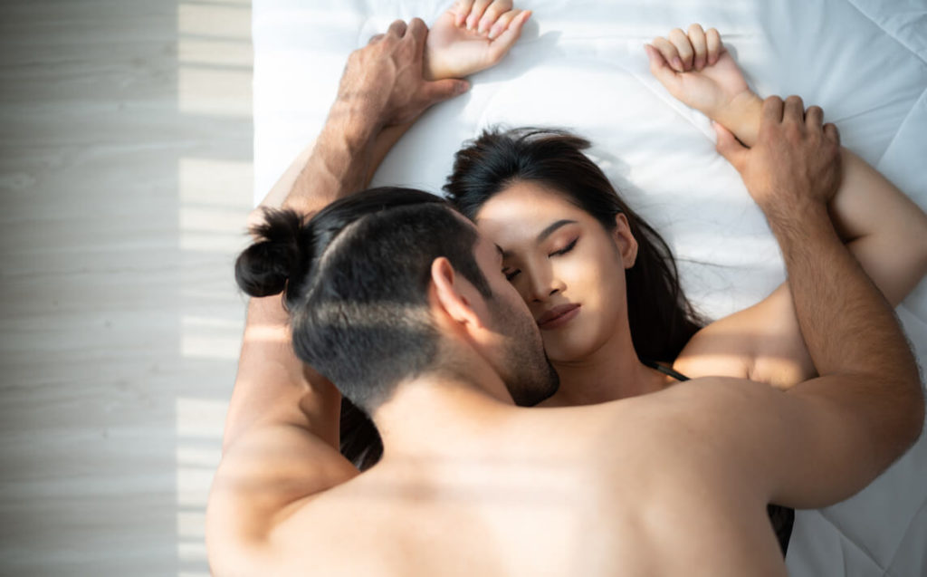 un homme aux cheveux attachés tient les deux mains d'une femme pendant qu'ils sont au lit et rencontrent au hasard