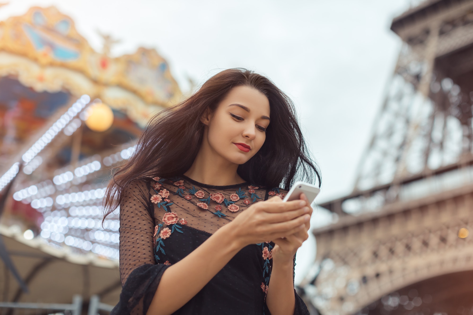 Femme en voyage utilisant un smartphone près de la Tour Eiffel et du carrousel, Paris