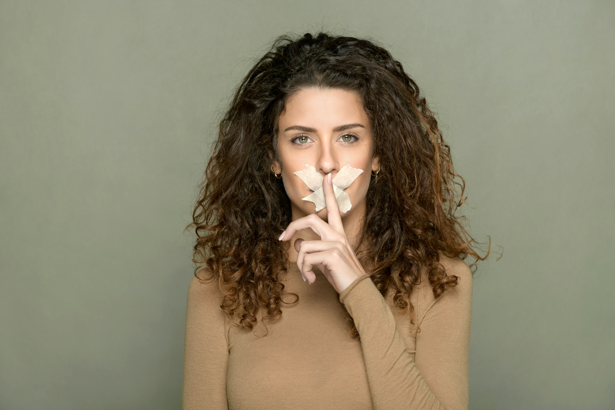 Une femme avec du ruban adhésif sur les lèvres fait la démonstration d'un geste de silence.