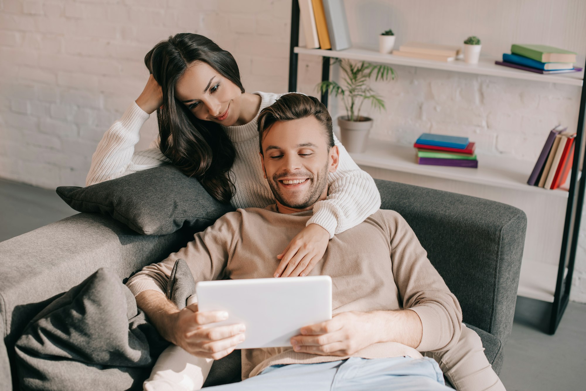 Jeune couple souriant utilisant une tablette sur le canapé à la maison.