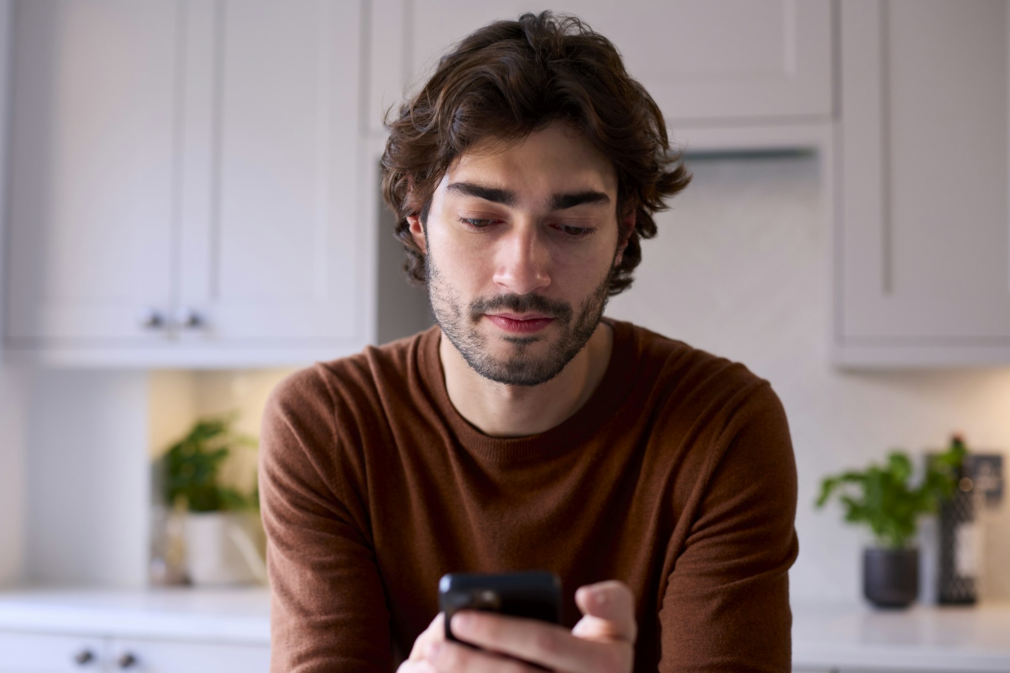 Un jeune homme se détend dans sa cuisine en consultant les messages des médias sociaux sur son téléphone portable.