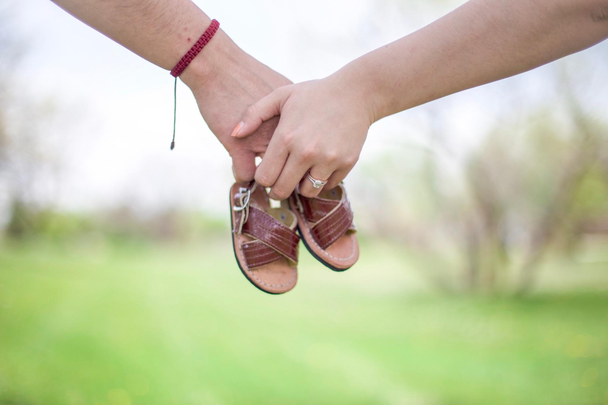 Un couple se tenant par la main et portant des chaussures de bébé pour annoncer leur grossesse.