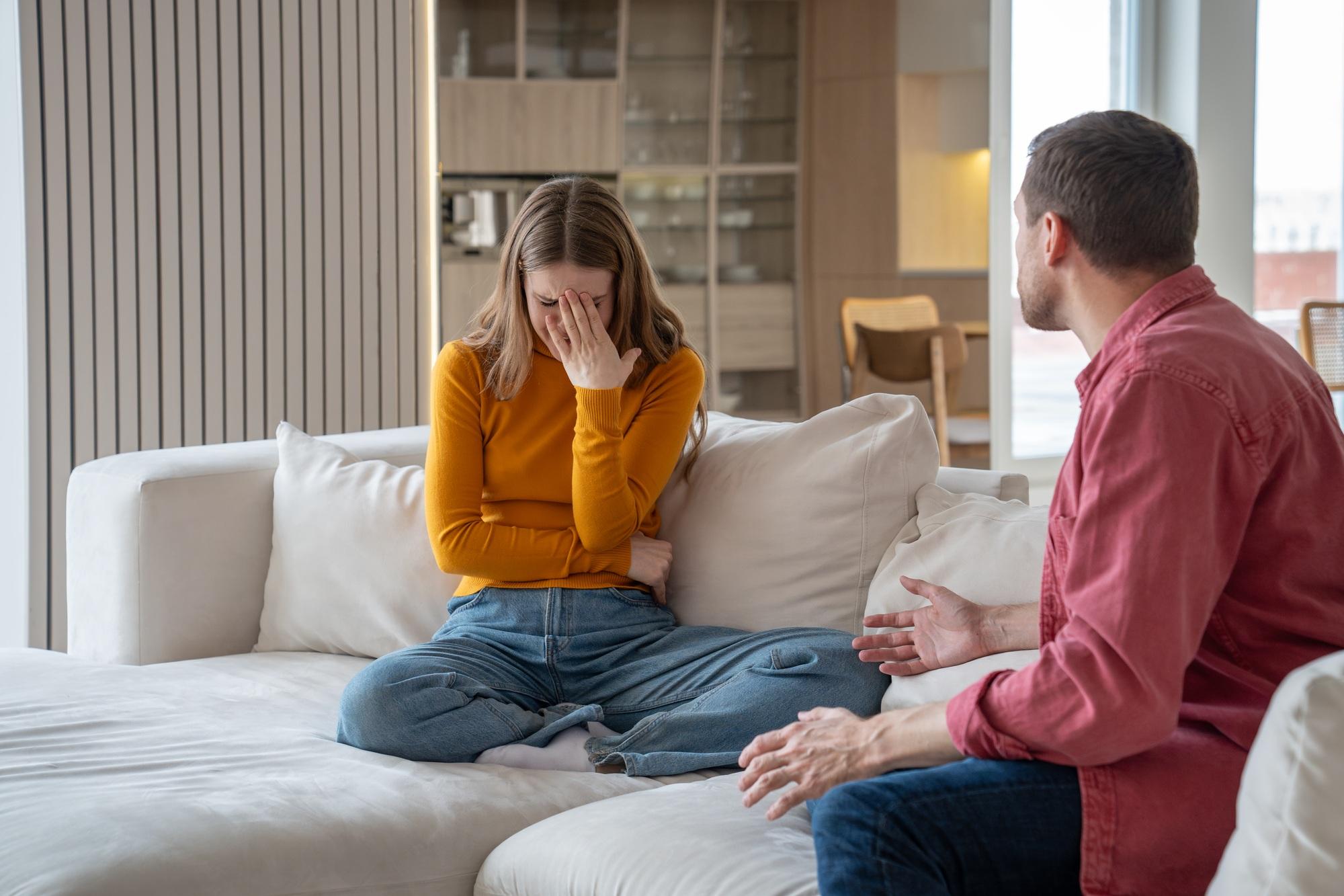 Une femme malheureuse et désemparée pleure en parlant au mari d'un homme cruel dans une relation abusive alors qu'elle est assise sur un canapé.