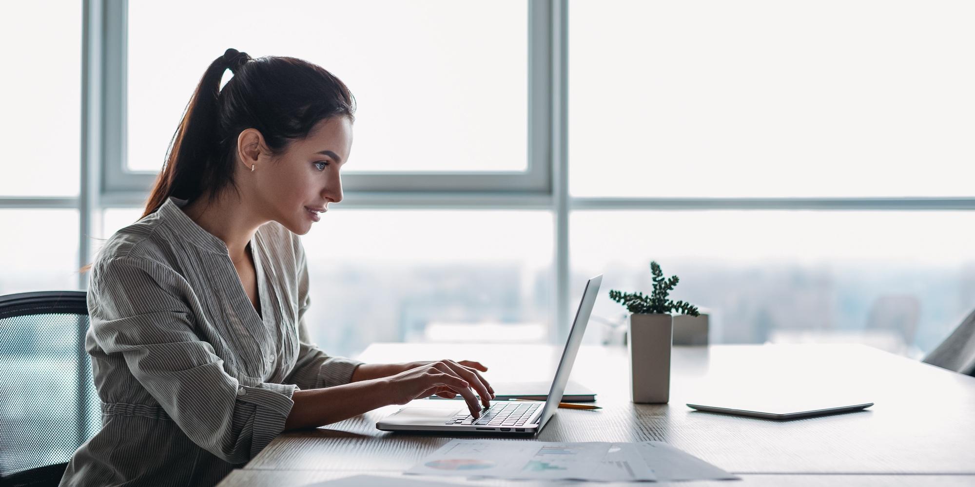 Titre du site : portrait d'une jeune femme magnifique et souriante utilisant un ordinateur portable au travail.