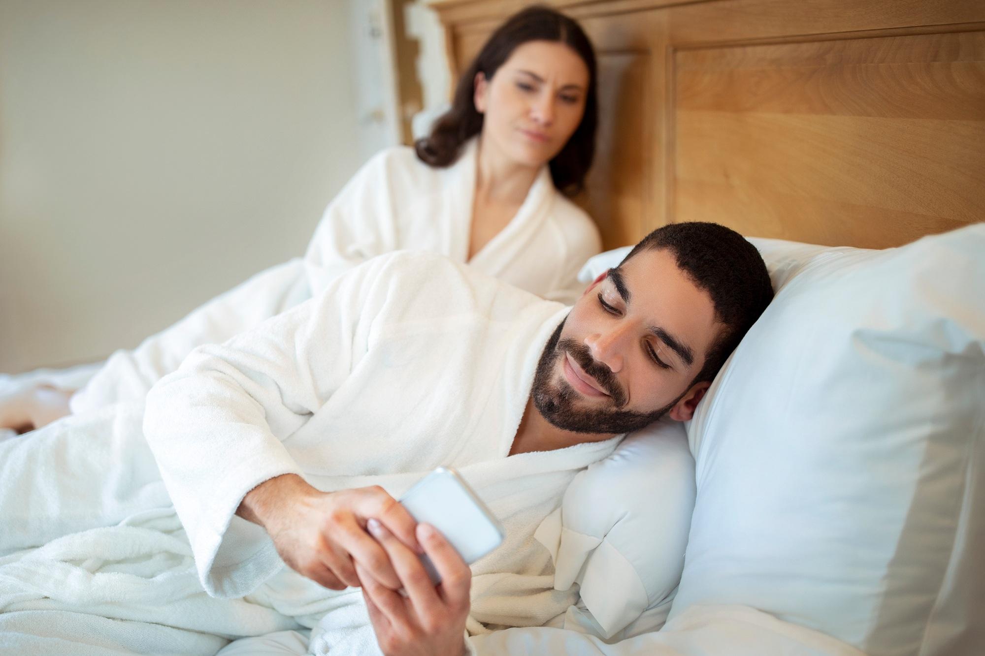 Une femme observe son mari pendant qu'il envoie des textos et doute de sa relation à l'intérieur.