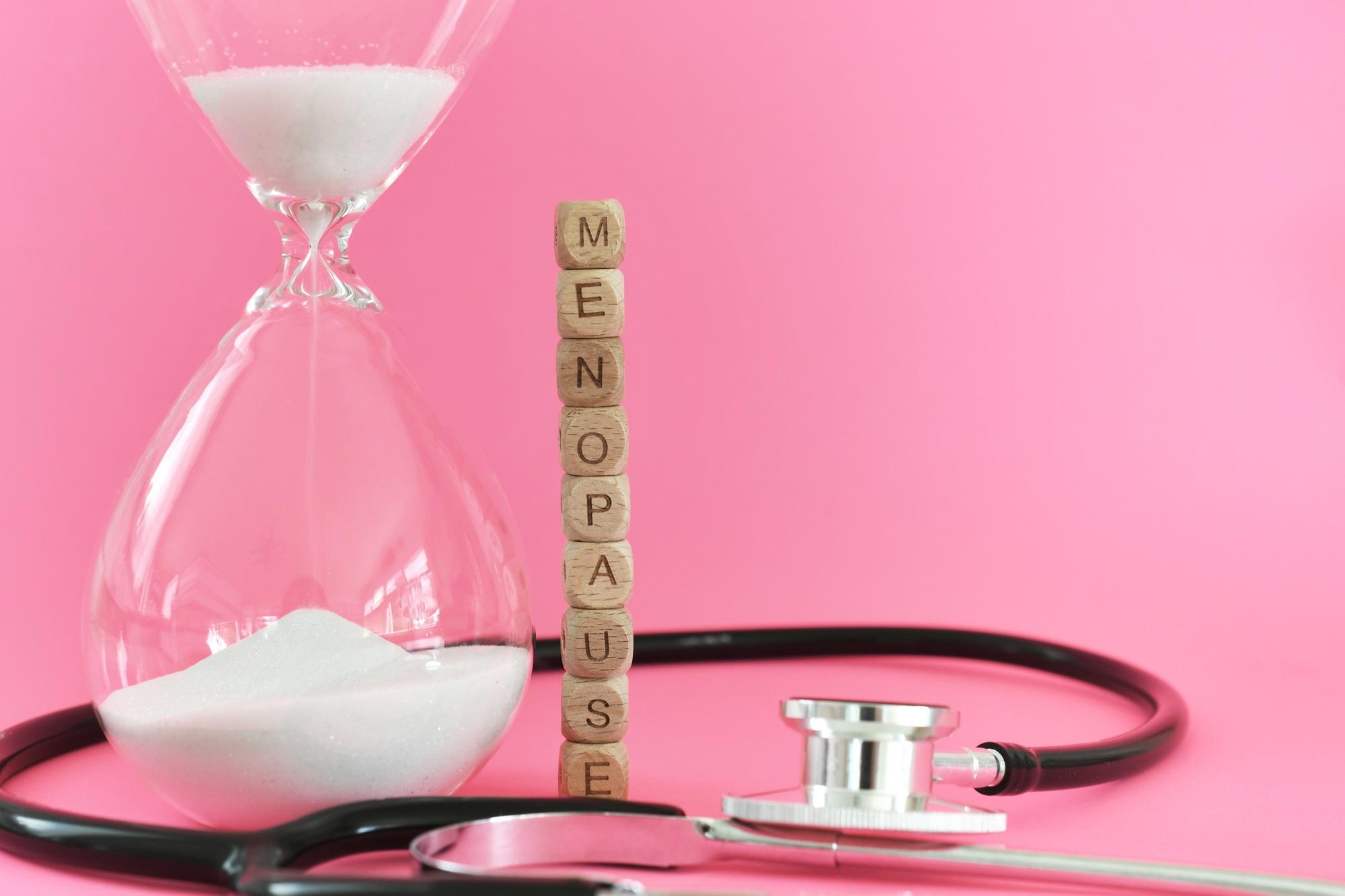 Ménopause avec stéthoscope et sablier sur fond rose. La ménopause est une période de changement.