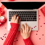 Valentines Day concept. Female hands typing on the keyboard, top view on pink background. Top view o