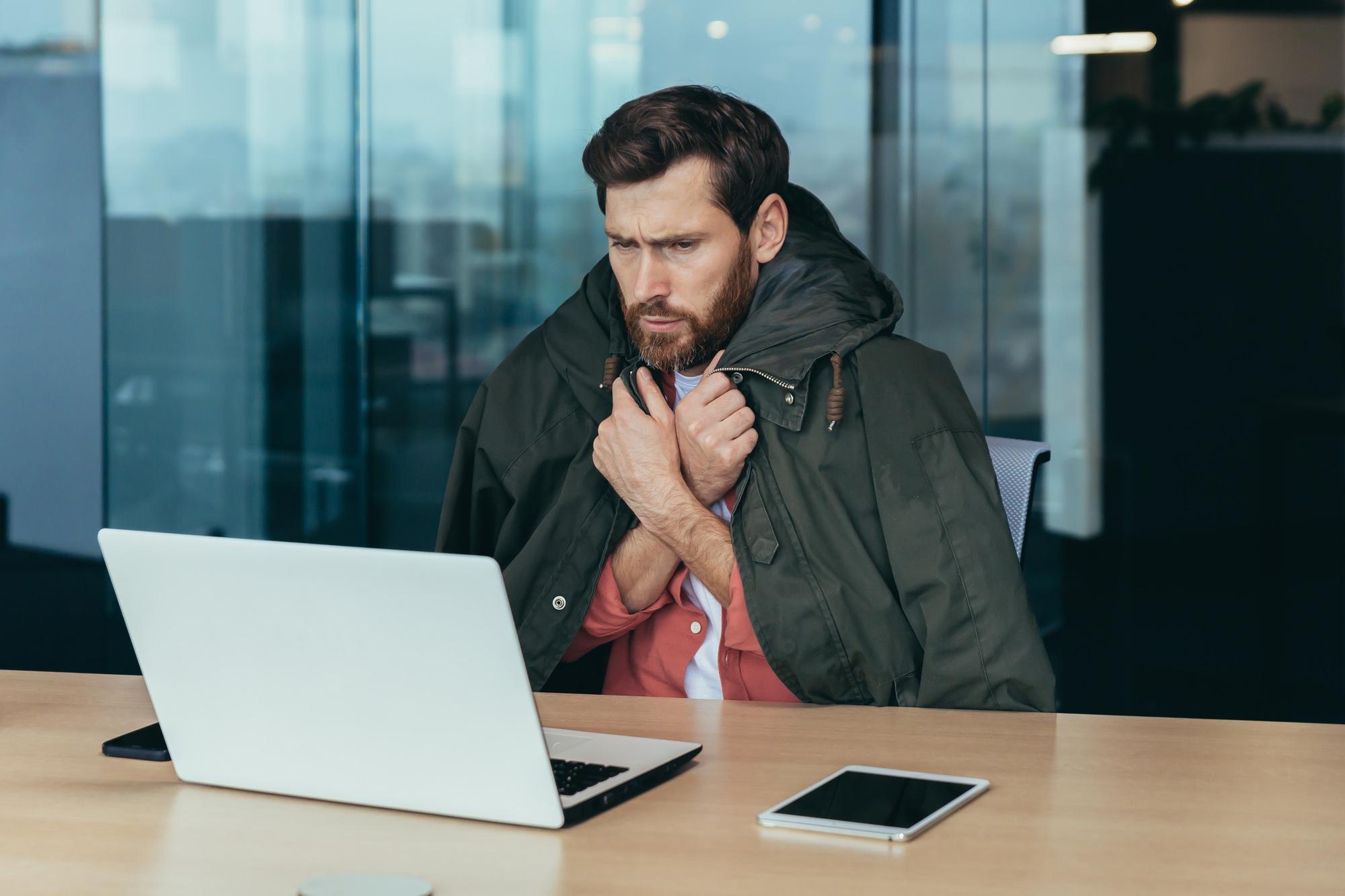 Il fait froid au bureau, un homme d'affaires gèle alors qu'il travaille sur son ordinateur portable à l'intérieur du bâtiment.