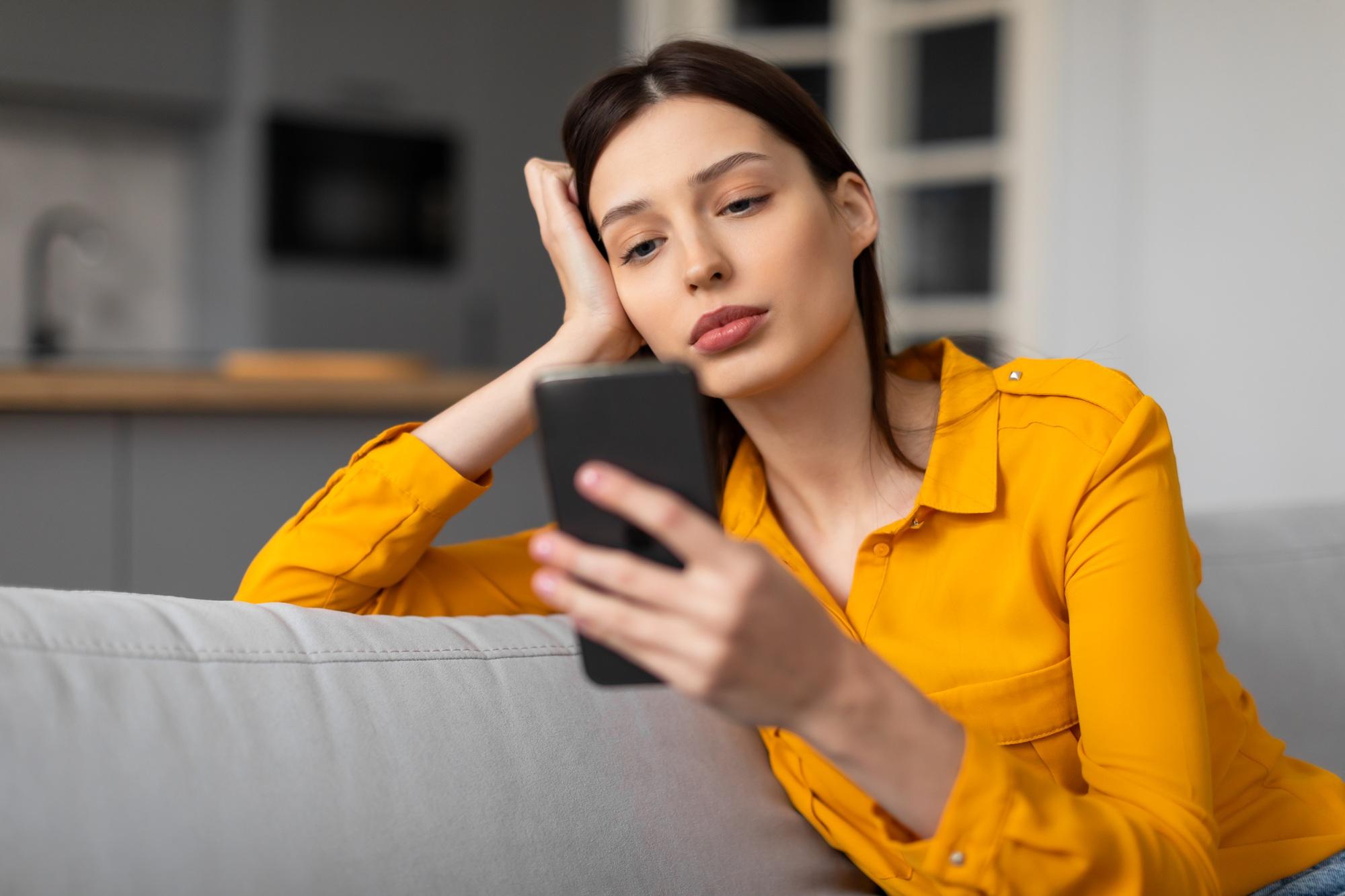 Une femme contemplative avec un téléphone a l'air triste et pensif sur un canapé.