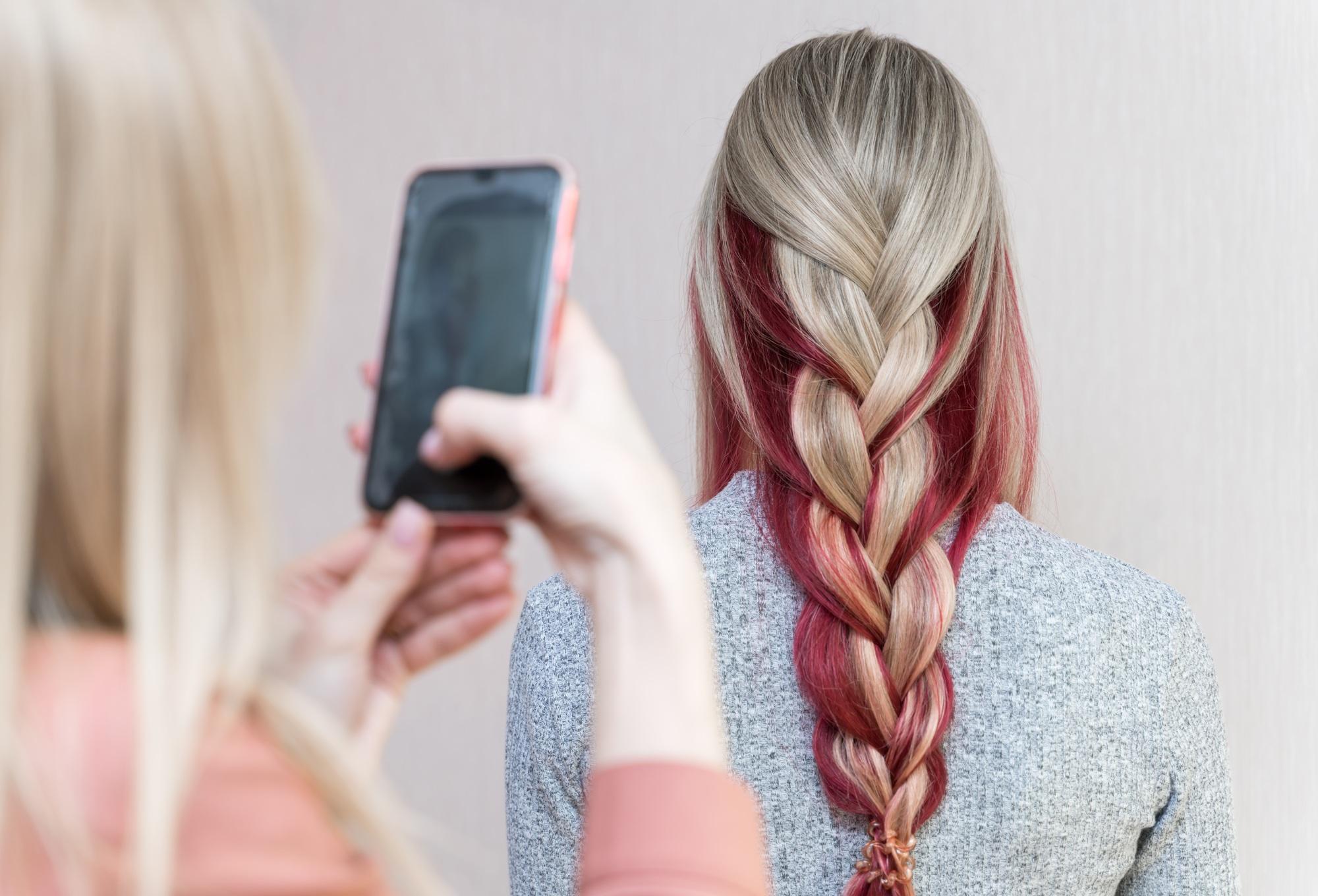 Un coiffeur photographie la coiffure d'une fille - cheveux longs tressés en une natte multicolore.
