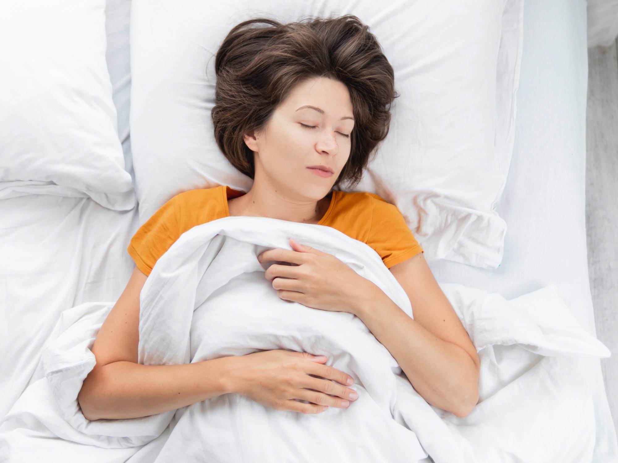 Vue de dessus d'une femme blanche dormant dans son lit. Sommeil profond sur une literie blanche.